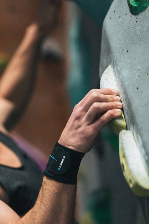 A man on a climbing wall, wearing the Compex Activ'® Wrist Band+ Support