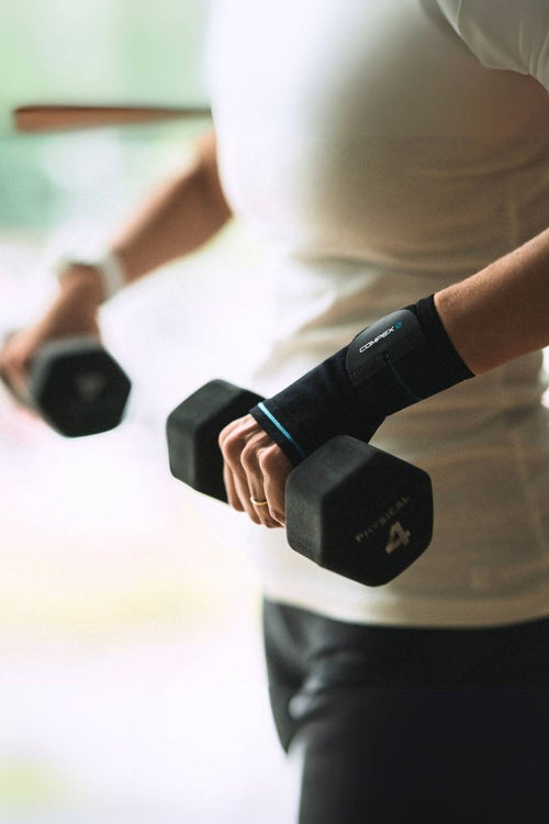 A woman lifting dumbbells, wearing the Compex Activ'® Wrist+ Support