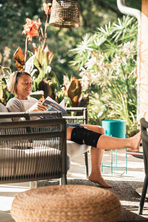 A woman relaxing with the Compex ComfortTENS Knee on her knee