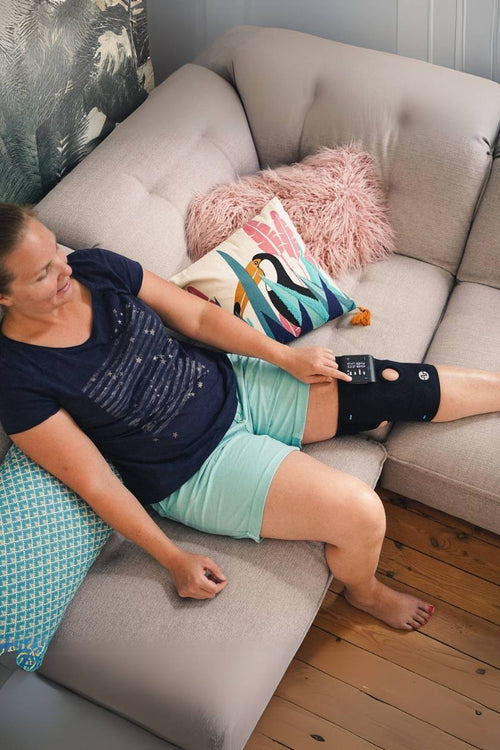 A woman relaxing on the sofa with the Compex ComfortTENS Knee on her knee