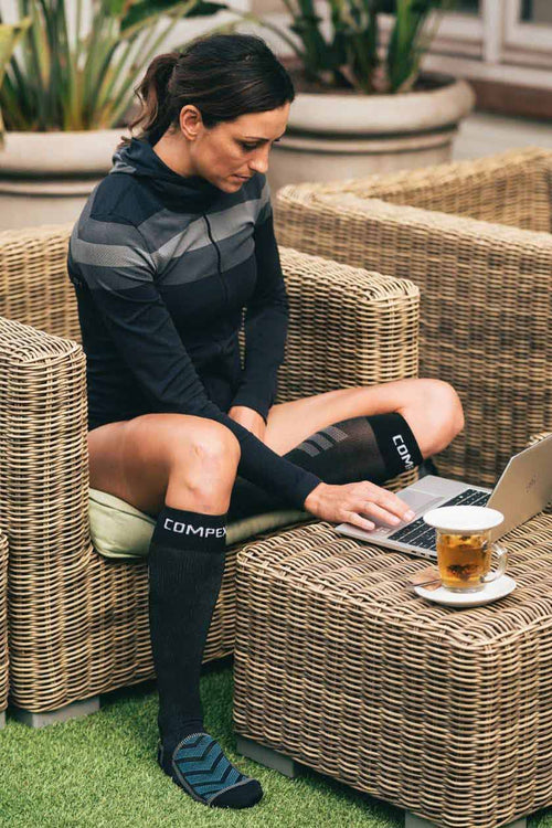 A woman sitting outside using her laptop, wearing the Compex Recovery Socks