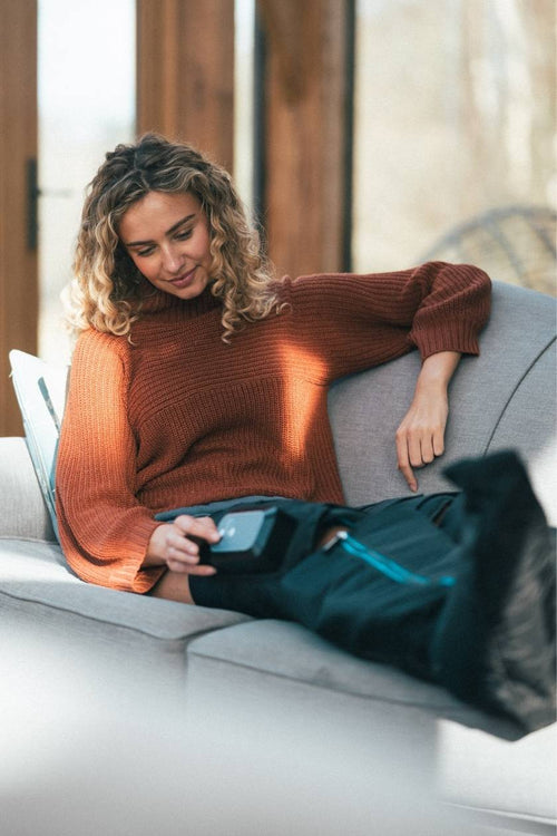 A woman relaxing on the sofa using the Compex Ayre wireless compression boots
