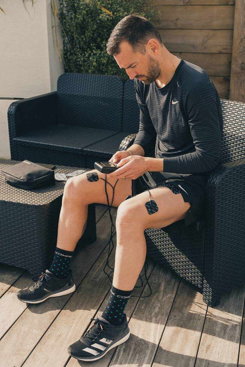 A man using the Compex Runner EMS muscle stimulator for a recovery session on his quad muscles