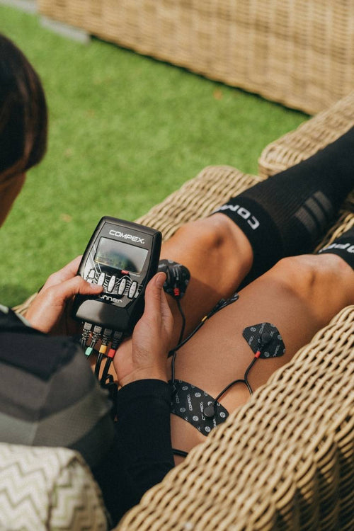 A woman using the Compex Runner EMS muscle stimulator for a recovery session on her quads