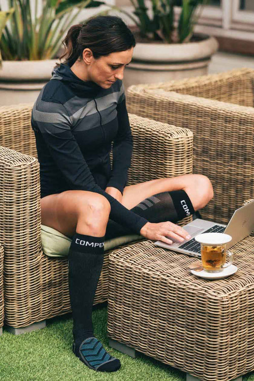 A woman sitting outside on her laptop wearing the Compex Recovery Socks