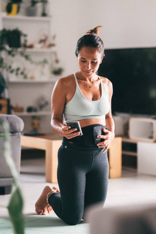 A woman using the Compex Corebelt EMS muscle stimulator to tone her abs