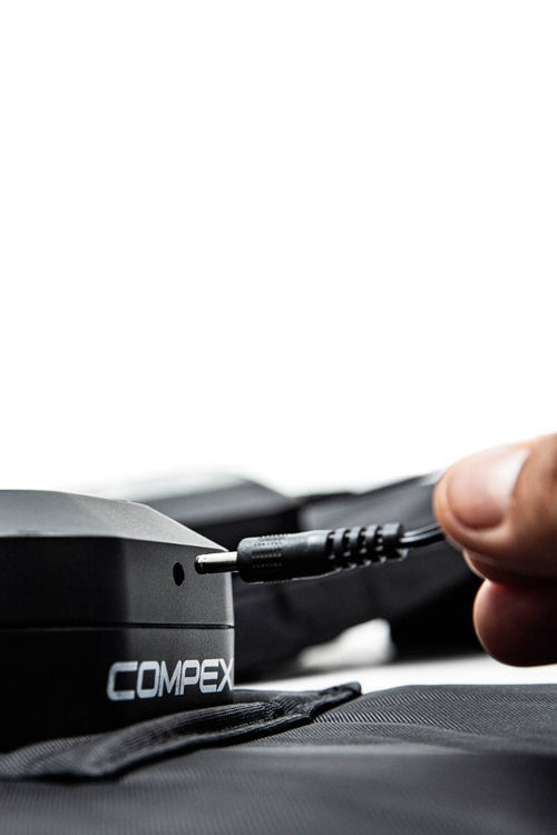 A man plugging in the charger for the Compex Ayre™ wireless compression boots