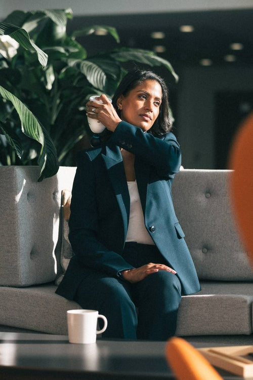 A woman sitting in a lobby using the Compex Fixx™ Mini massage gun on her shoulder