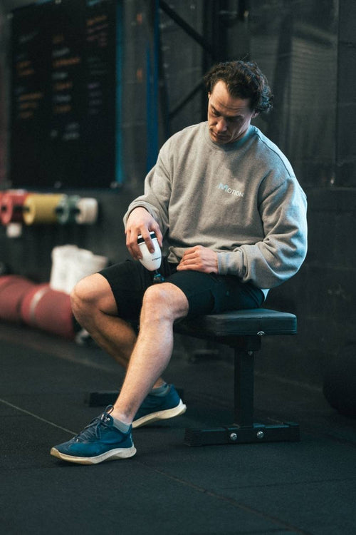 A man sitting in a gym, using the Compex Fixx™ Mini massage gun on his quad muscles