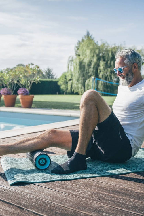 A man massaging his calf muscle using the Compex Ion™ vibrating massage roller
