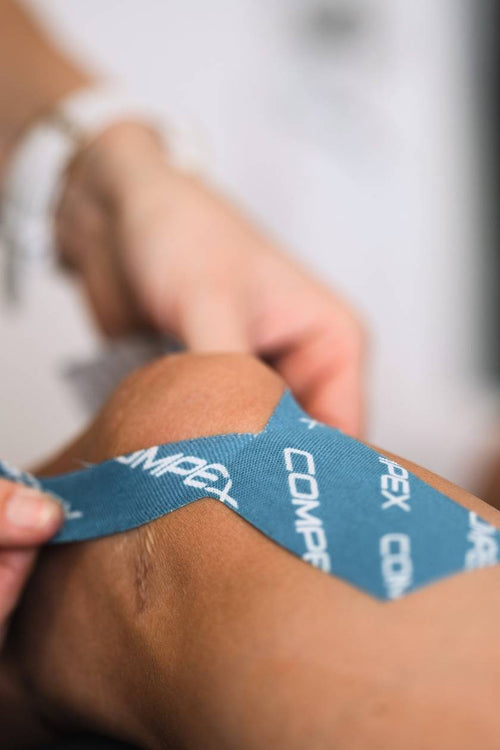 A woman applying blue Compex K-Tape to her knee