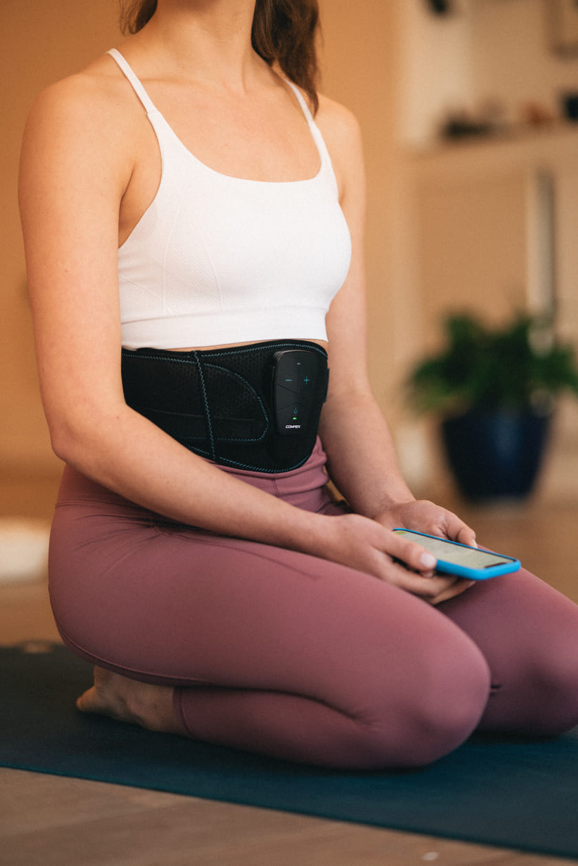 A woman using the Compex Corebelt EMS muscle stimulation belt to flatten her stomach