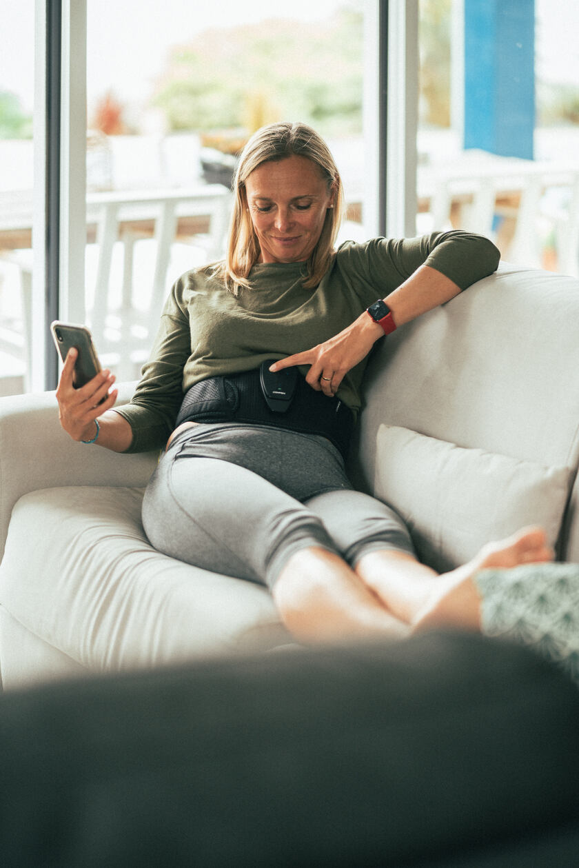 A woman turning on the Compex Corebelt EMS muscle stimulator belt