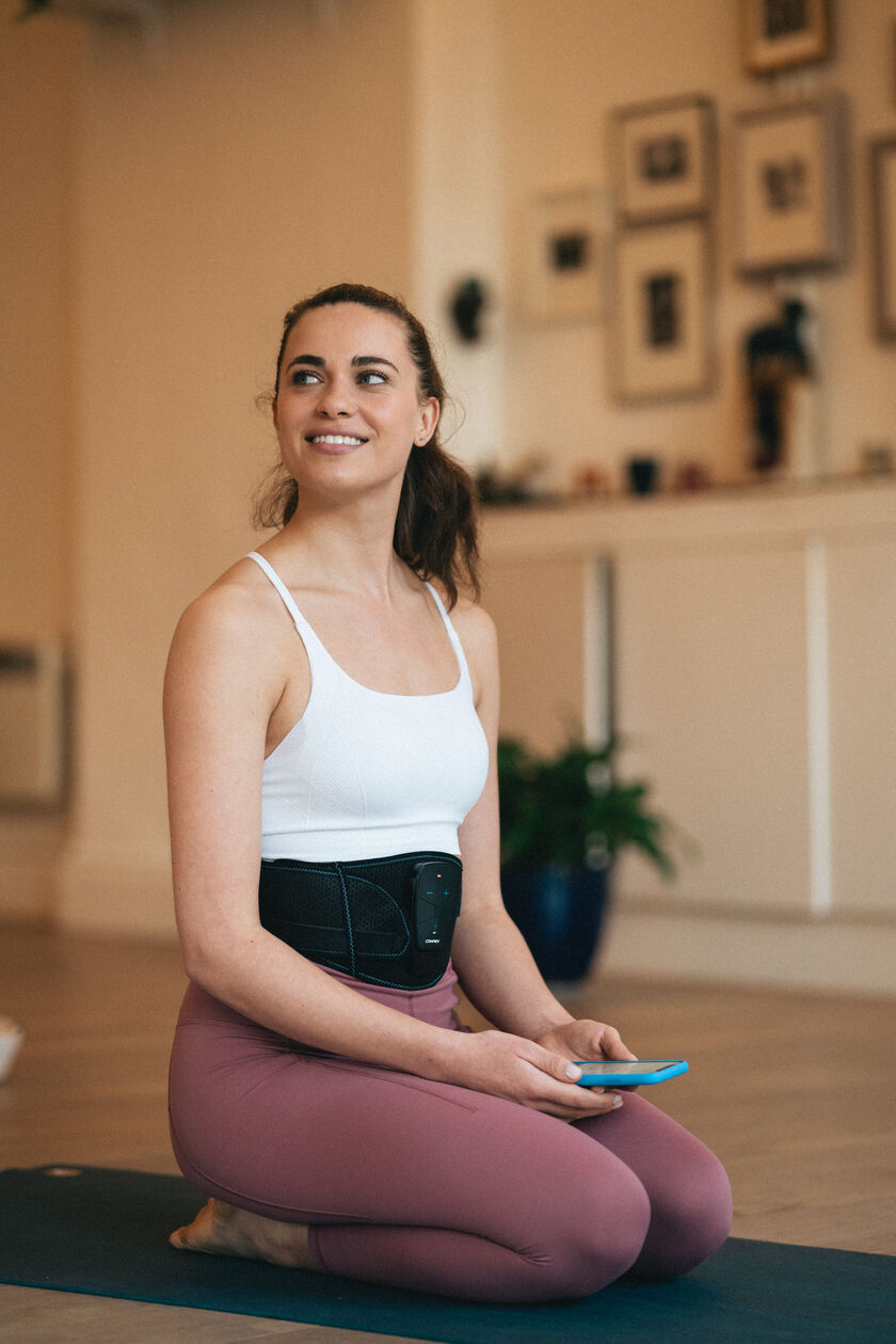 A woman using the Compex Corebelt EMS muscle stimulator belt