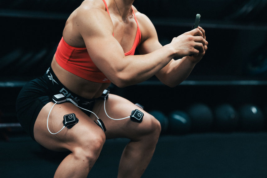 A woman doing a squat using the Compex Ulitmate Pro EMS device as part of her strength and conditioning program