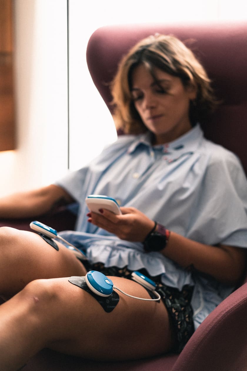 A woman using the Compex FIT 5.0 EMS muscle stimulator to relax her quad muscles
