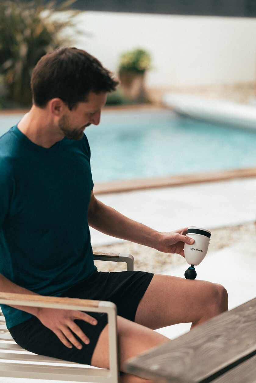 A man using the Compex Fixx Mini massage gun on his quads
