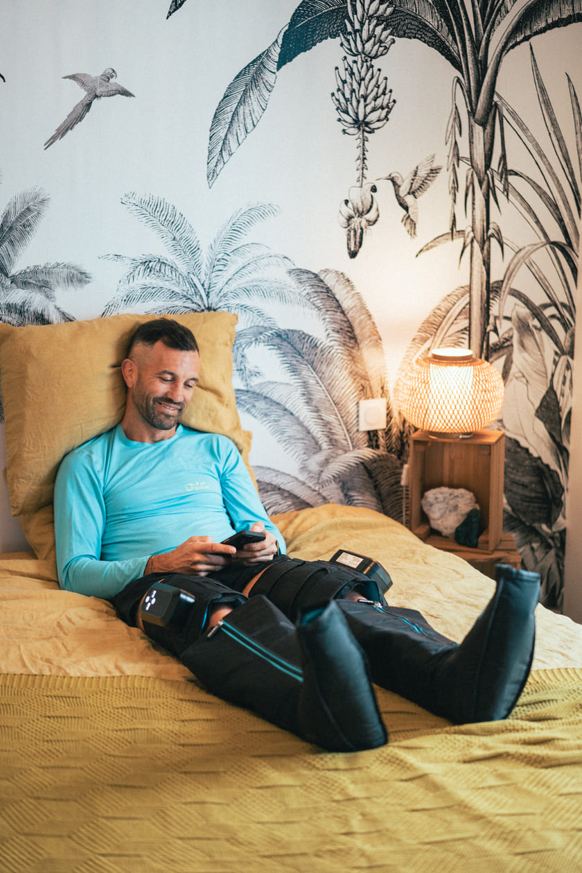 A man relaxing in bed using the Compex Ayre™ compression boots