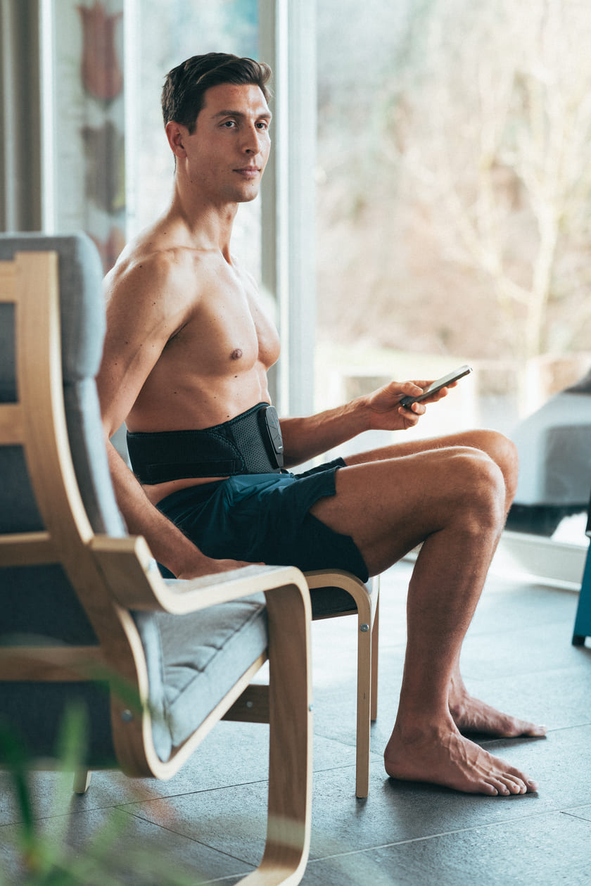 A man sitting down using the Compex Corebelt EMS muscle stimulator belt