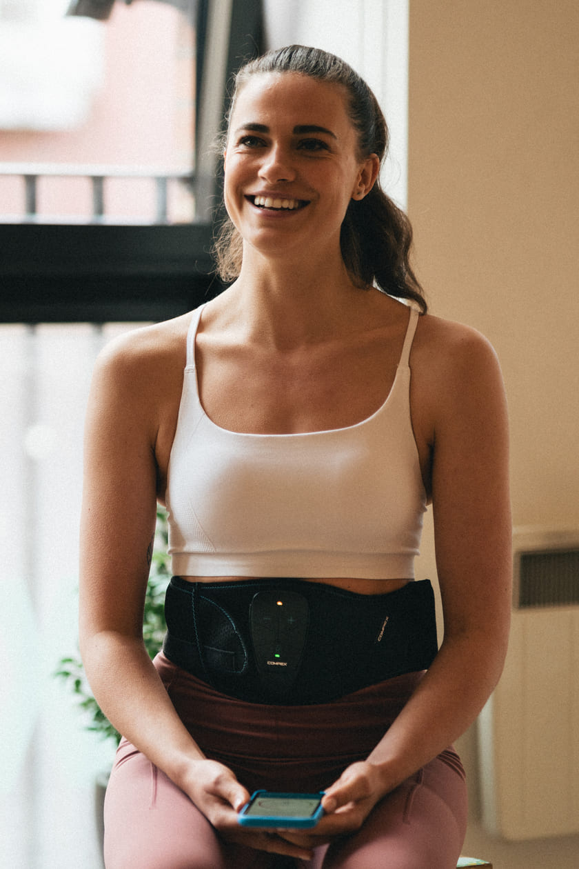 A woman using the Compex Corebelt EMS muscle stimulator belt