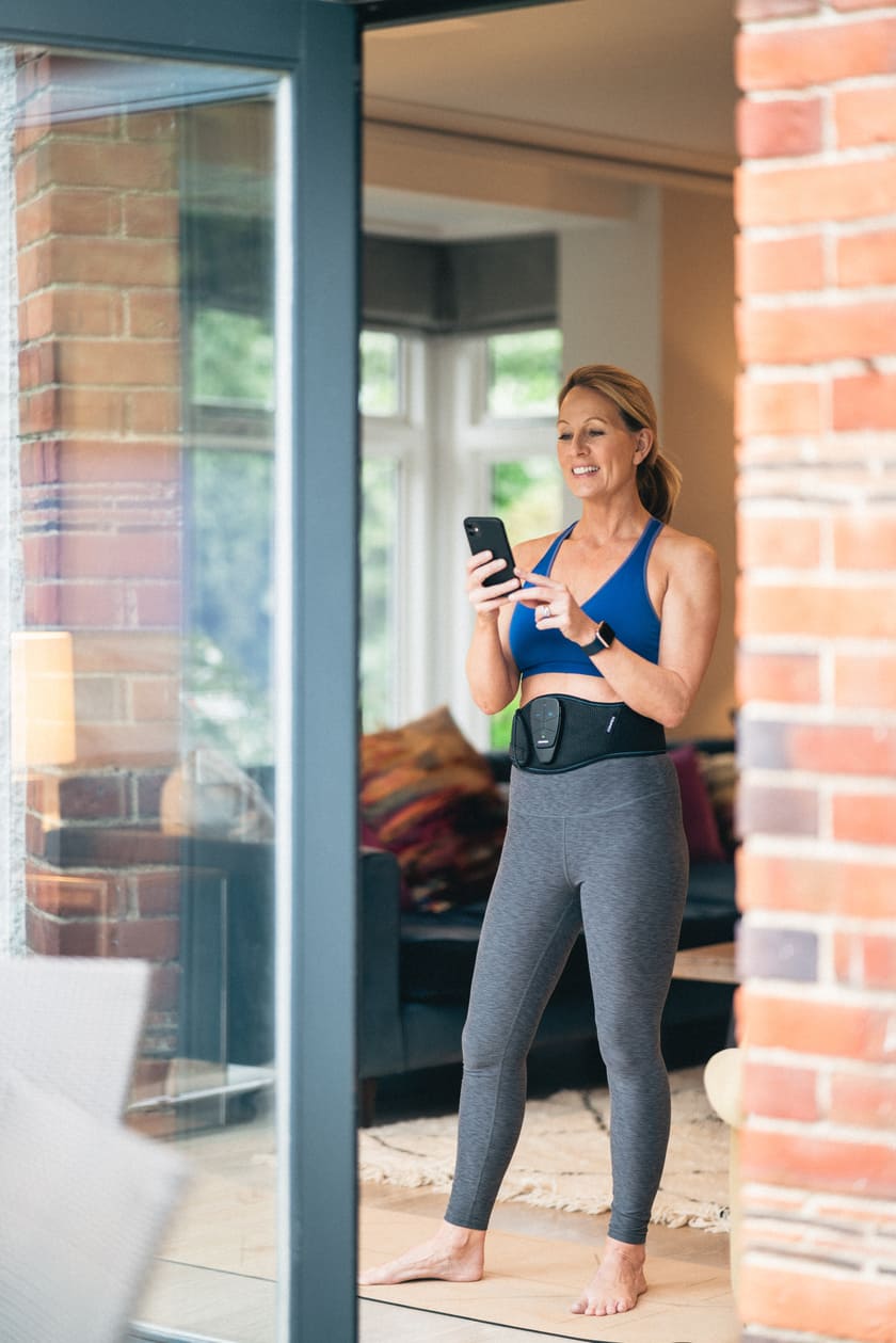 A woman using the Compex Corebelt EMS muscle stimulator belt