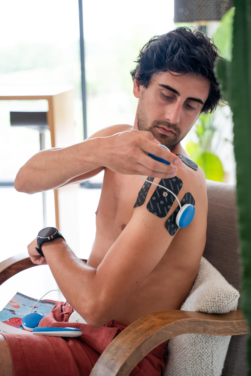 A man relieving shoulder pain using the Compex FIT 5.0 EMS muscle stimulator