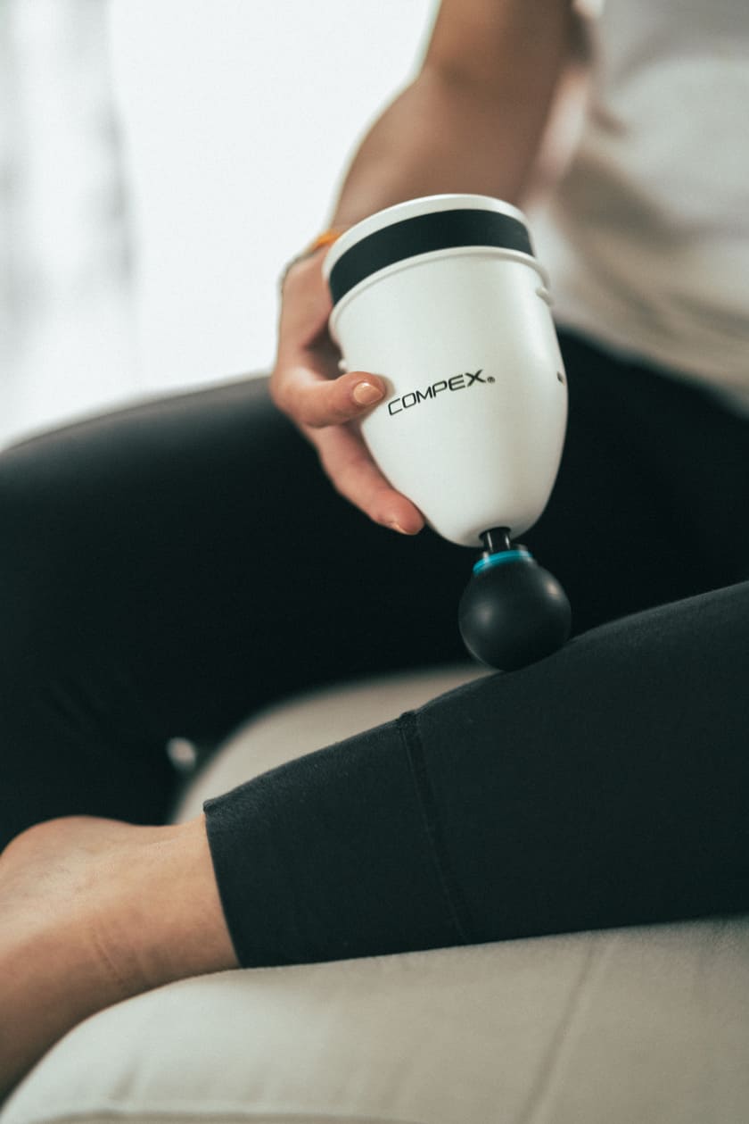 A woman massaging her calf muscles using the Compex Fixx™ Mini percussion massage gun