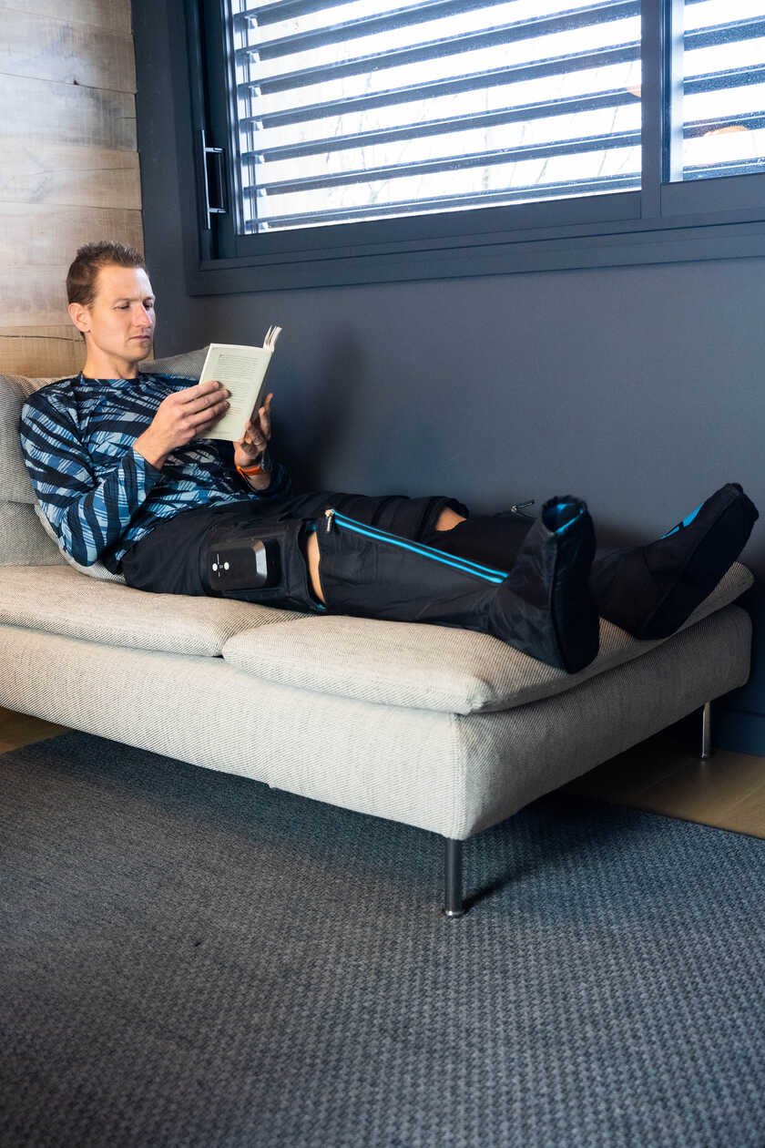 A man using the Compex Ayre wireless compression boots while reading a book