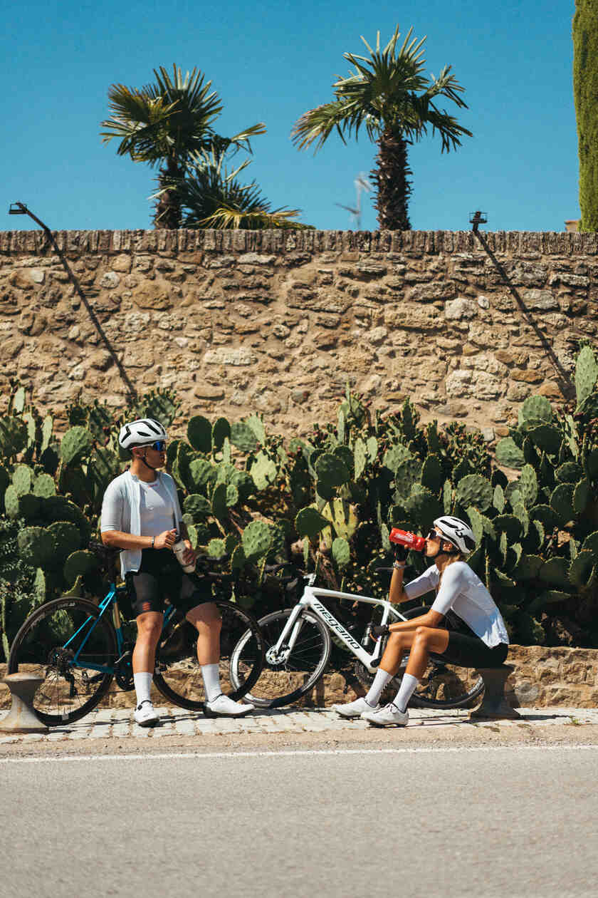Two cyclists taking a drinks break at the side of a road