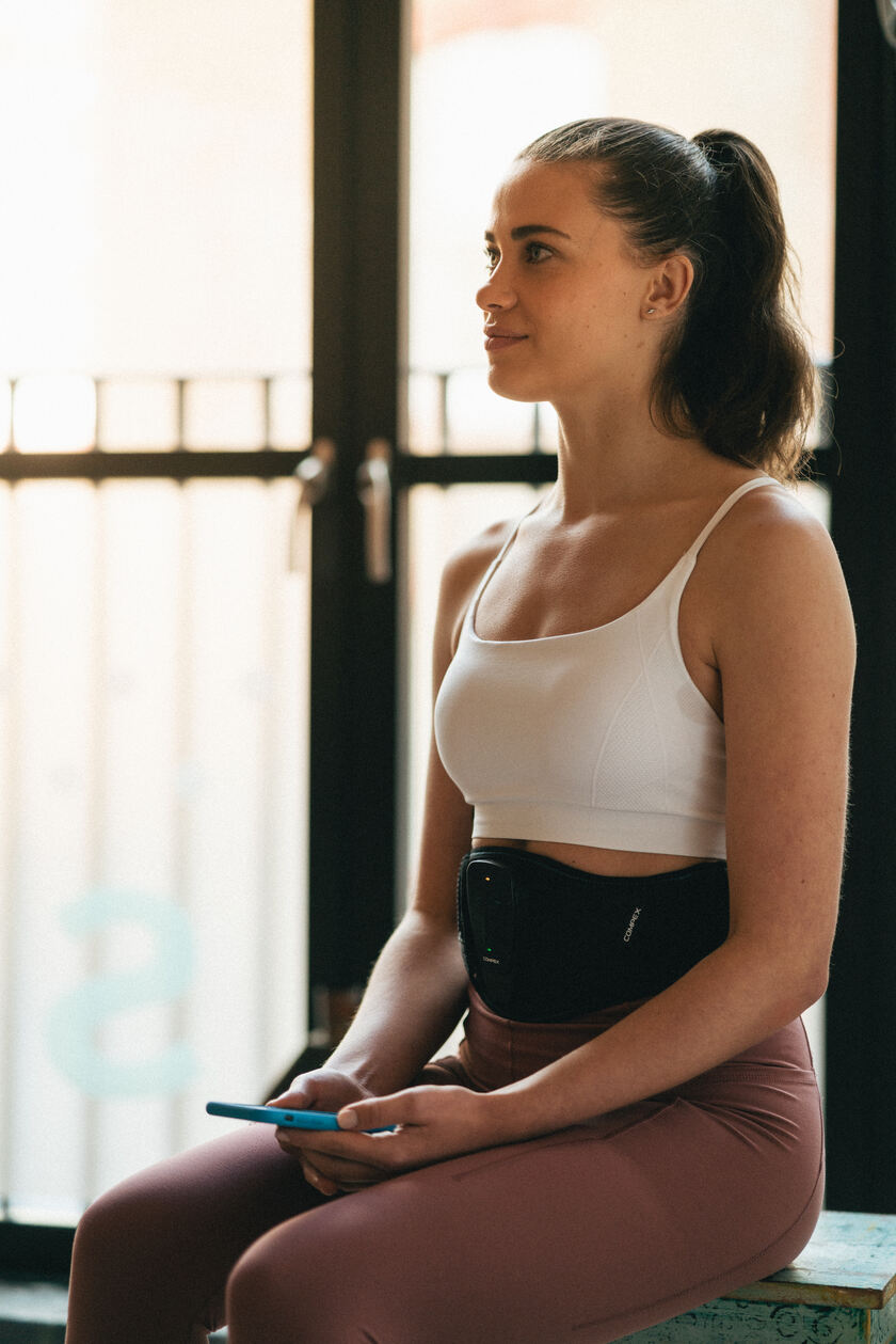 A woman using the Compex Corebelt EMS muscle stimulator belt
