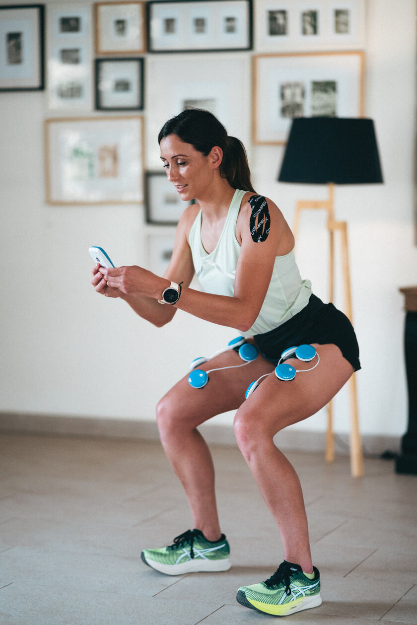 A womman doing a squat using the Compex FIT 5.0 EMS muscle stimulator