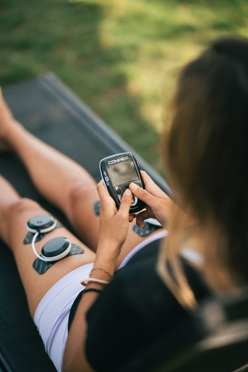 A woman using the Compex SP 8.0 EMS muscle stimulator to do recovery on her quads