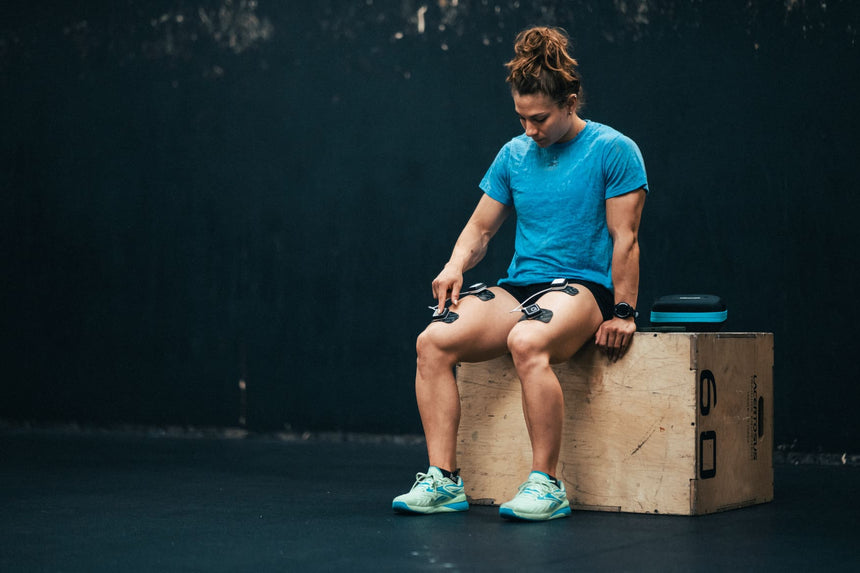 A woman using the Compex Ultimate EMS device to do a recovery session on her quadricep muscles