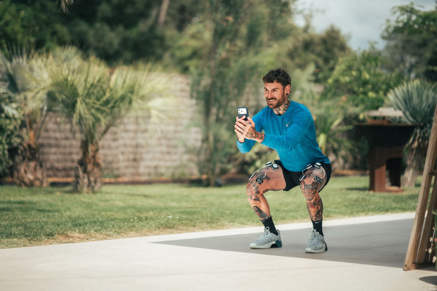 A man doing a squat using the Compex Ulitmate Pro EMS device as part of his strength and conditioning program