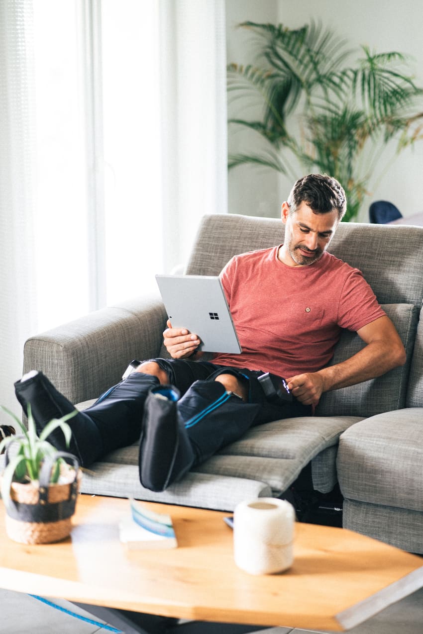 Man using a laptop on a couch using the Compex Ayre compression boots