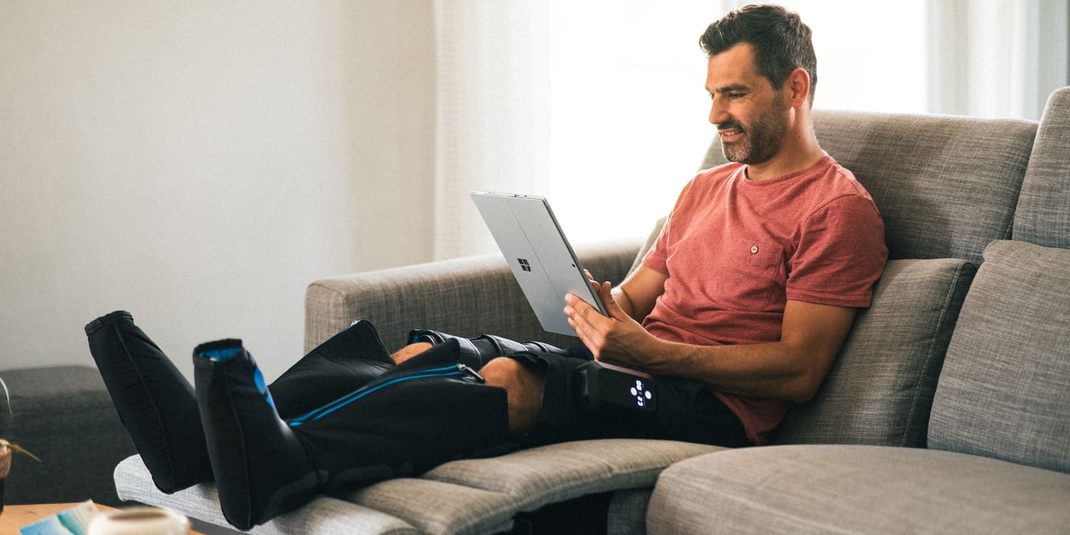 Man using a laptop on a couch using the Compex Ayre compression boots