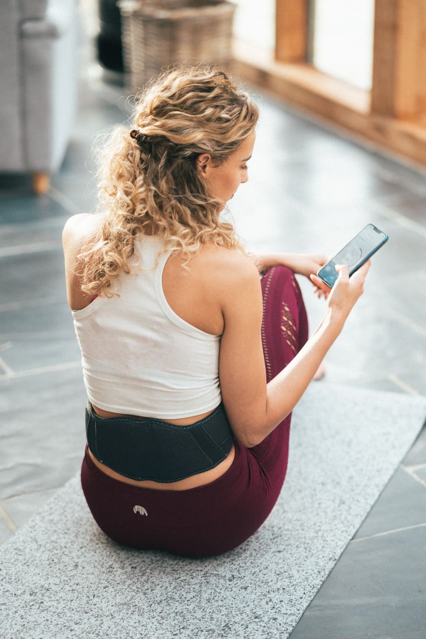 A woman sitting in her house using the Compex Corebelt app on her phone