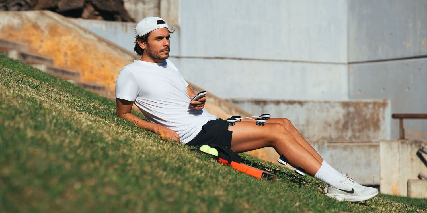 A padel player using the Compex SP 8.0 EMS muscle stimulator on his quad and calf muscles