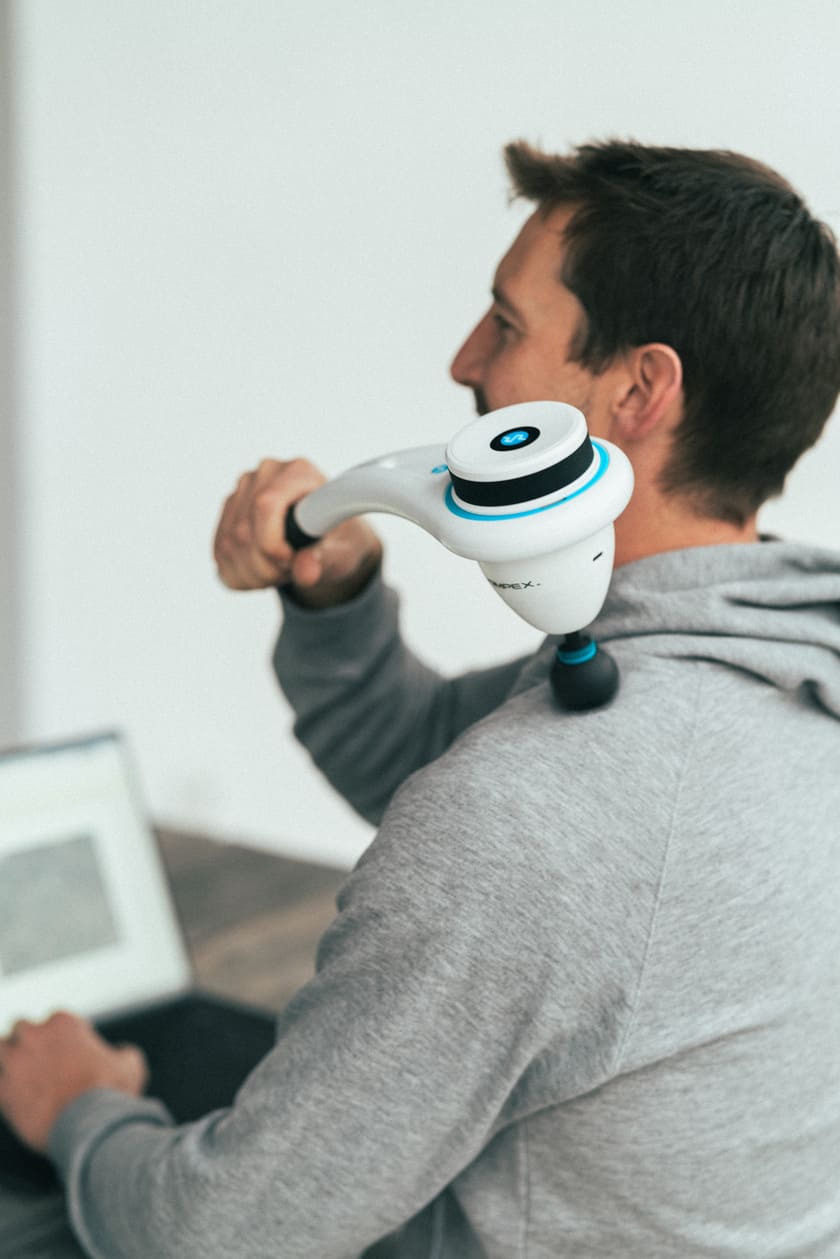 A man massaging his shoulder with the Compex Fixx Mini massage gun