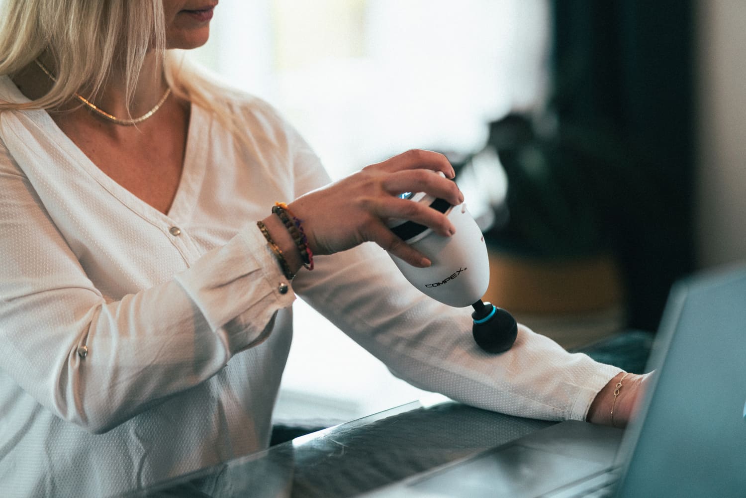 A woman using the Compex Fixx Mini massage gun for a forearm massage