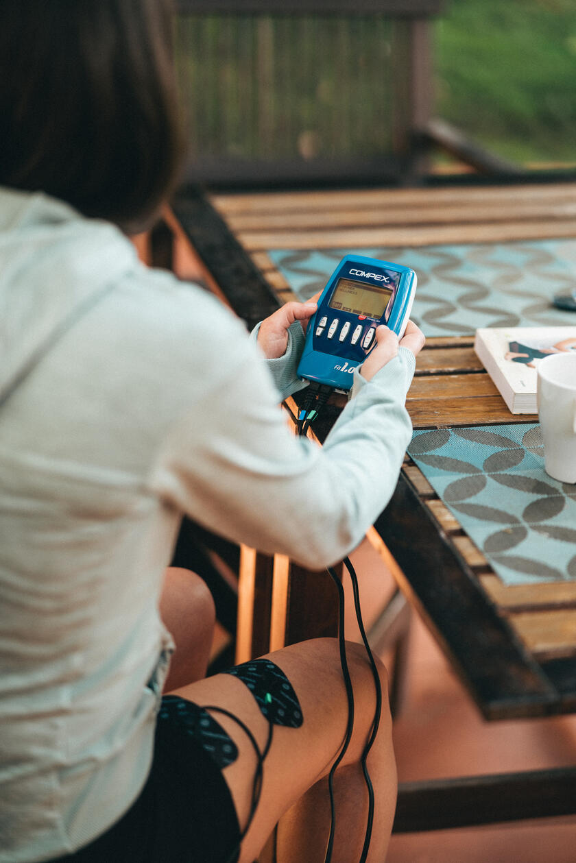 A woman using the Compex FIT 1.0 EMS muscle stimulator to do recovery on her quads