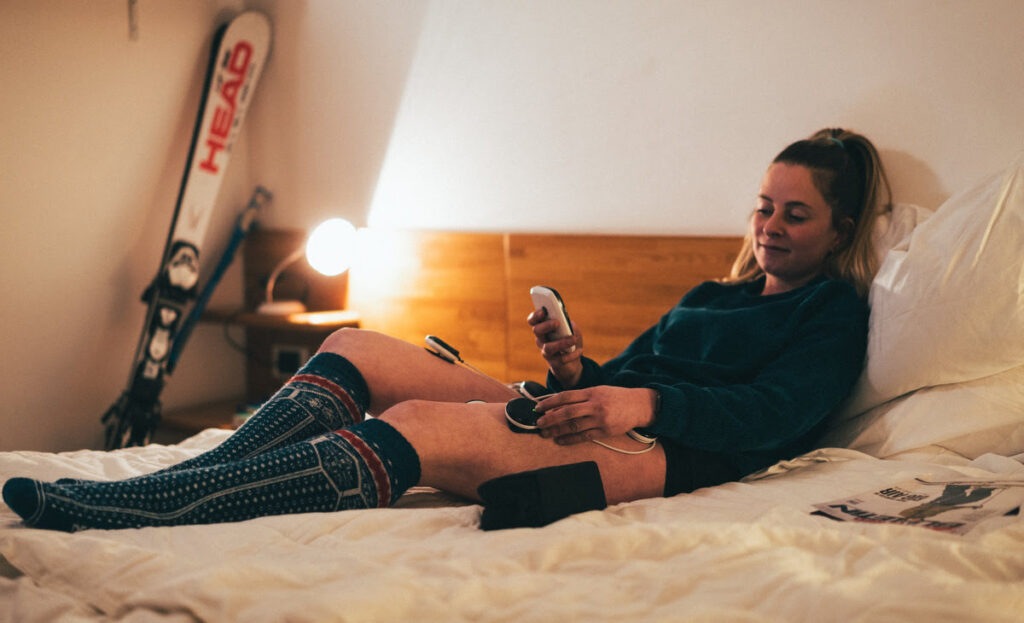 A woman laying in bed, with the Compex SP 8.0 providing muscle recovery