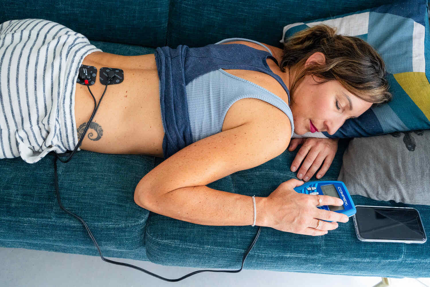 A woman treating her Lumbago using the Compex FIT 3.0 muscle stimulator