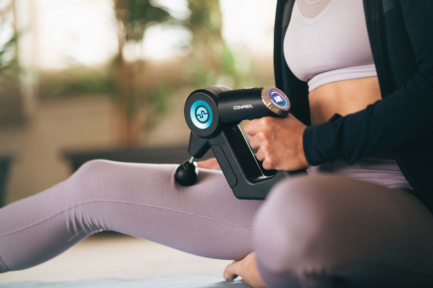 A woman using the Compex Fixx 2.0 massage gun to help relax muscles