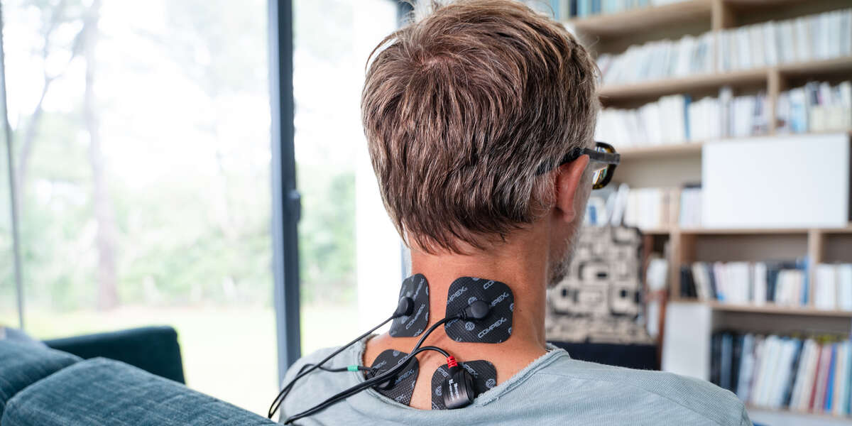 Een man krijgt een nekmassage met de Compex SP 4.0 elektrostimulator